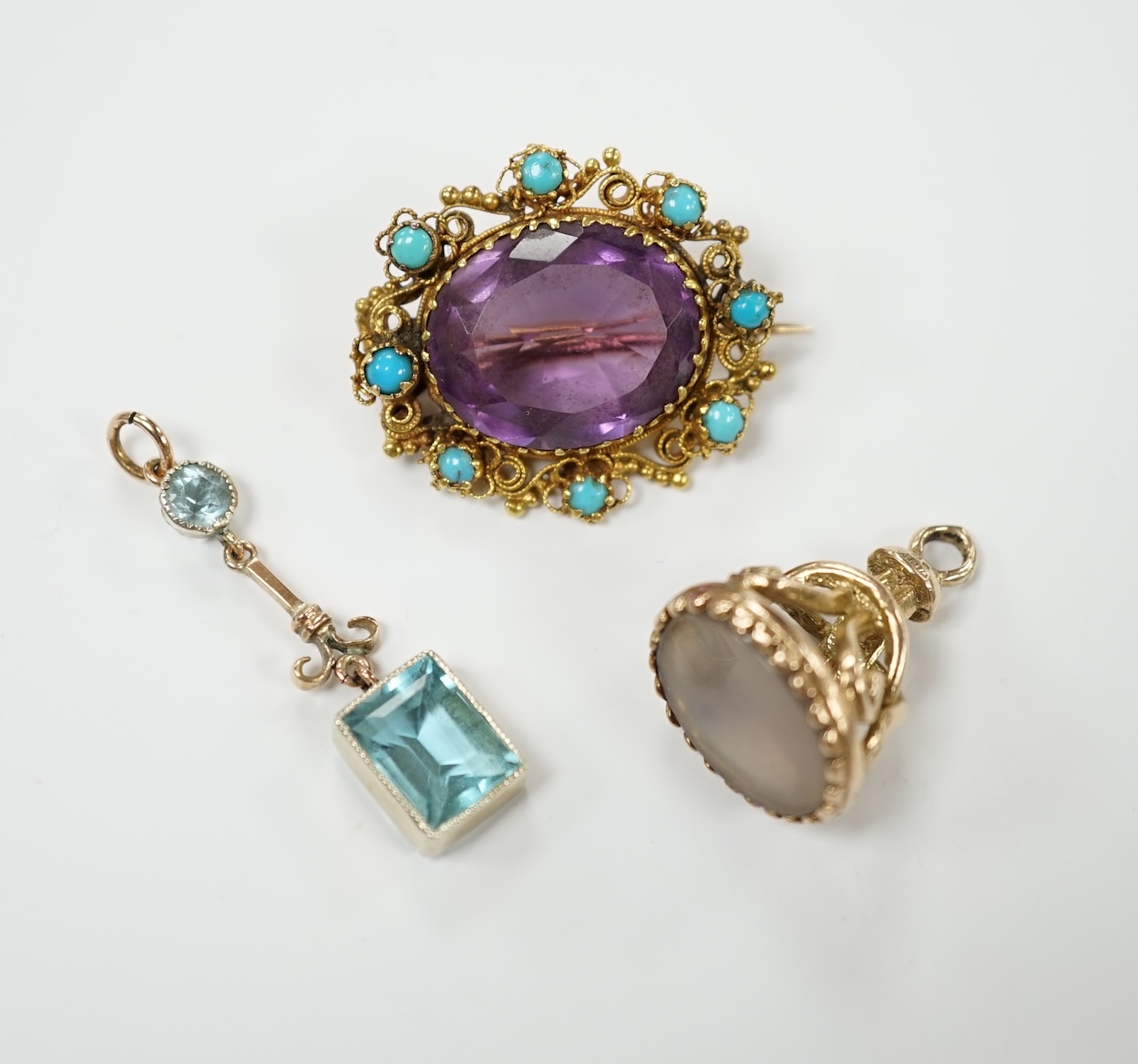 An early 20th century yellow metal, amethyst and turquoise set brooch, 25mm, a 9ct gold and white chalcedony set fob and a yellow metal and gem set drop pendant. Condition - poor to fair